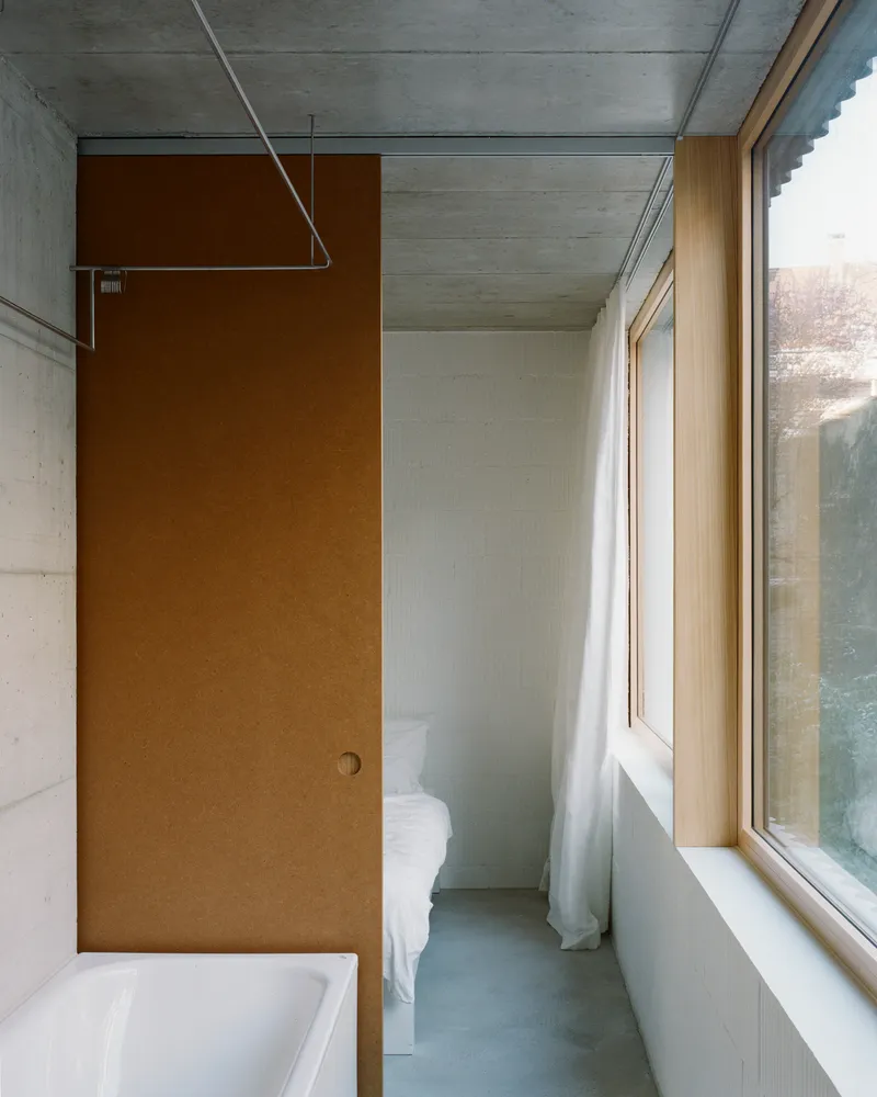 Compact bedroom with timber door and cast concrete ceiling beneath a window alcove