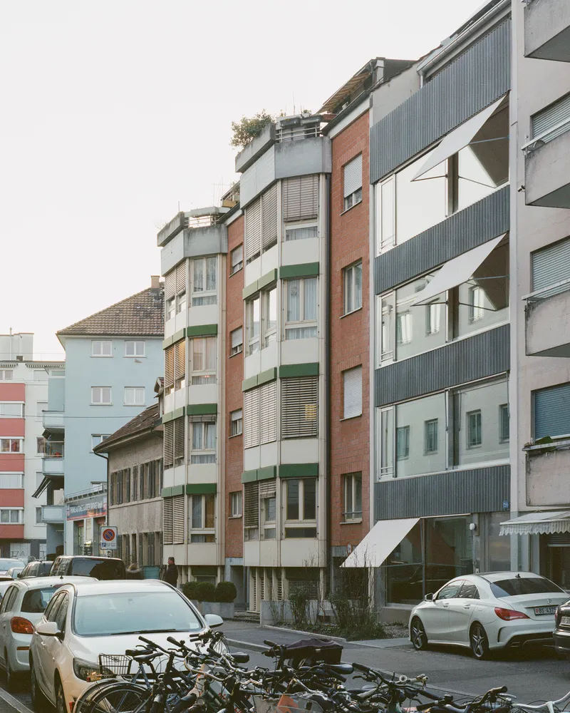 Streetscape showing a mix of residential buildings with metal cladding, brick and balconies with parked cars and bicycles