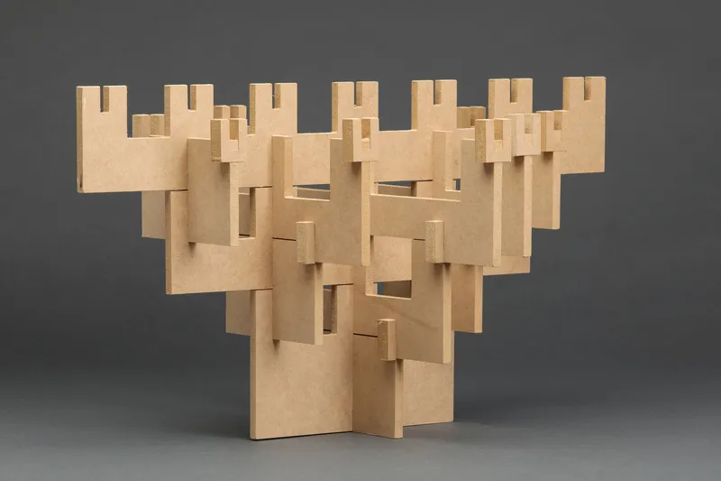 Cardboard study model showing interlocking vertical planes with notched apertures on grey backdrop