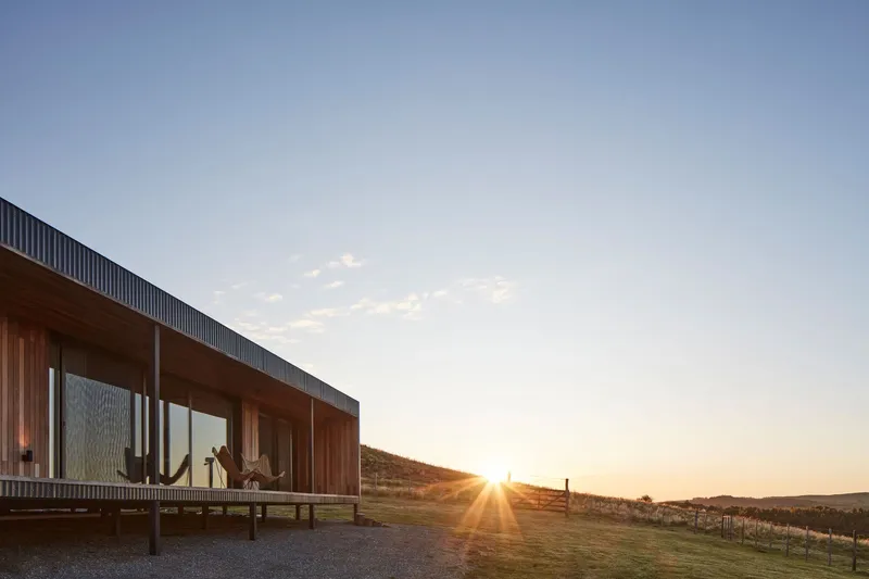 Timber deck and glazed facade with corrugated metal parapet catching low golden sunset light