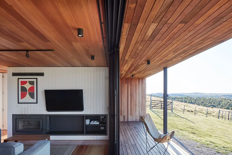Corner window opening onto a timber deck overlooking fenced pasture and distant hills