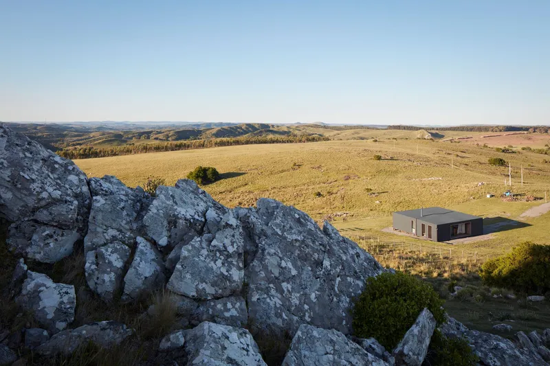 Distant view of the pavilion from rocky outcrops overlooking golden grassland at dusk