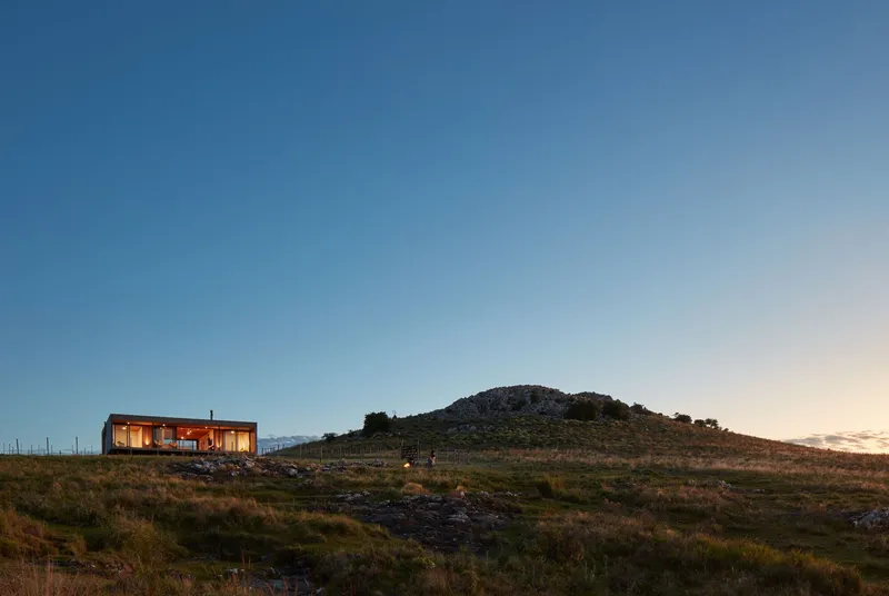 Long view of the illuminated glass volume on a hillside at twilight