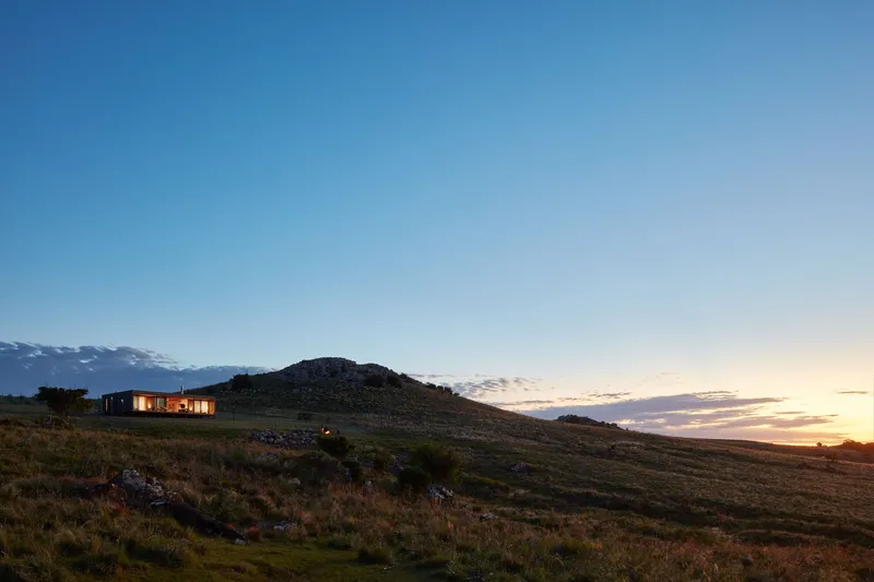 The lit pavilion nestled below a rocky hill as sunset colors fill the sky