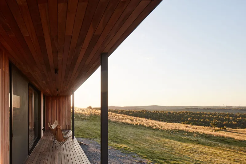 Covered timber deck with slatted ceiling and steel column overlooking rolling hills at golden hour