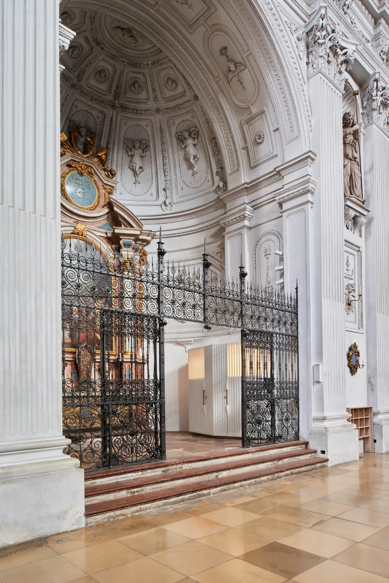 Curved white ribbed enclosure beneath a coffered dome with ornamental plasterwork and a gilded clock