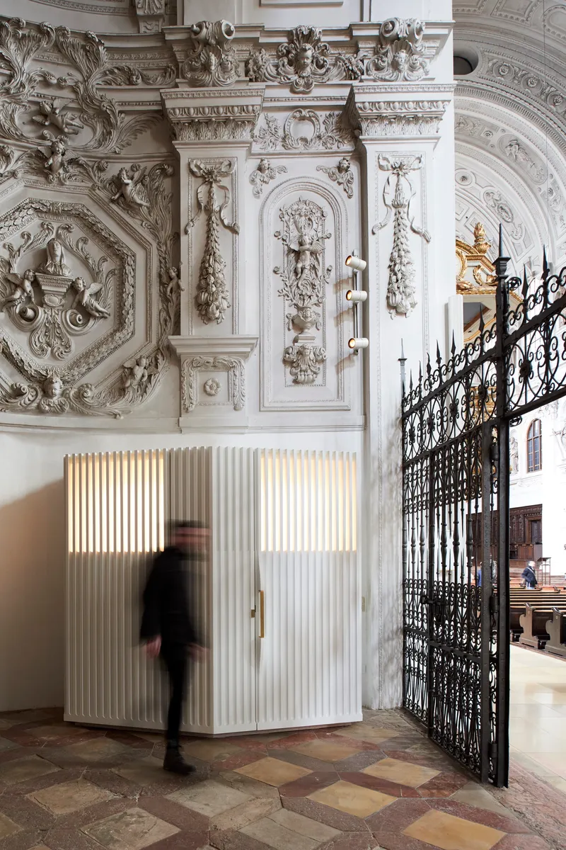 Corner of the white fluted timber booth with backlit panels as a figure passes in motion blur