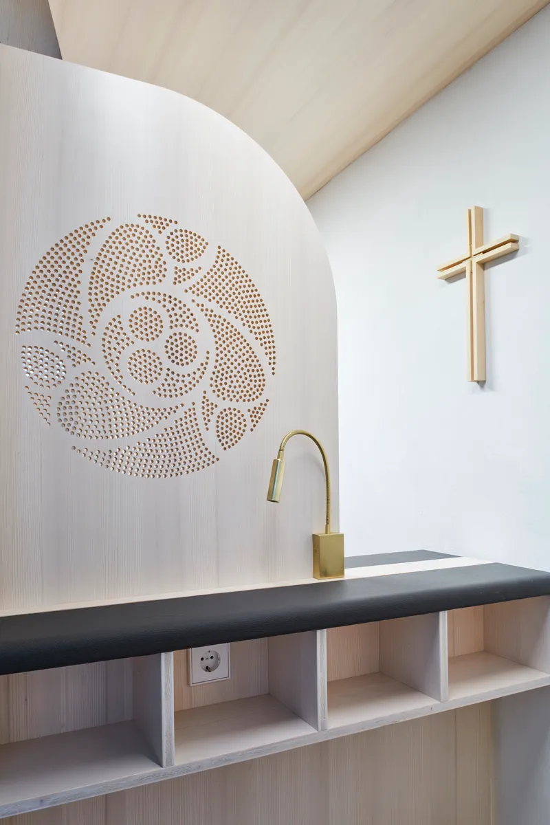 Close-up of the perforated white panel with decorative circular pattern above a dark upholstered bench and brass faucet
