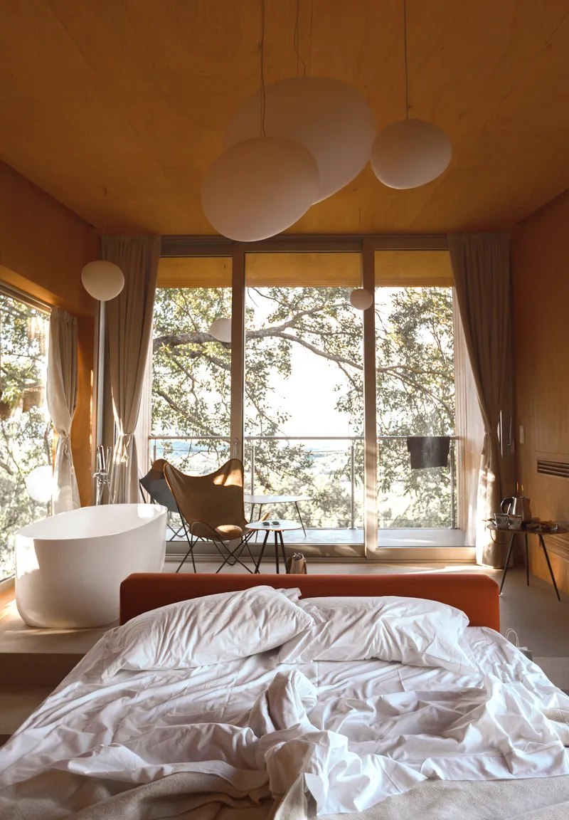 Bedroom with plywood ceiling, spherical pendant lights, and full-height glazing overlooking trees