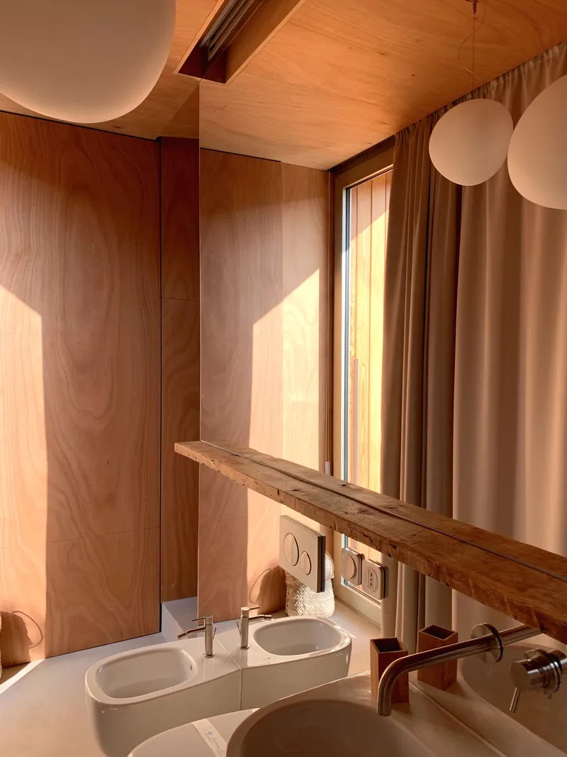 Bathroom with twin sinks below timber-framed mirror catching warm sunlight through linen curtains