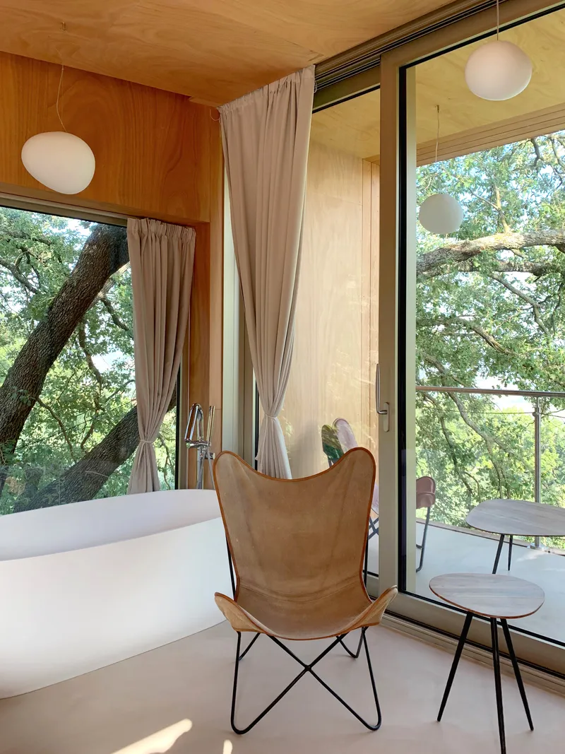 Corner room with floor-to-ceiling glazing opening to terrace among tree branches