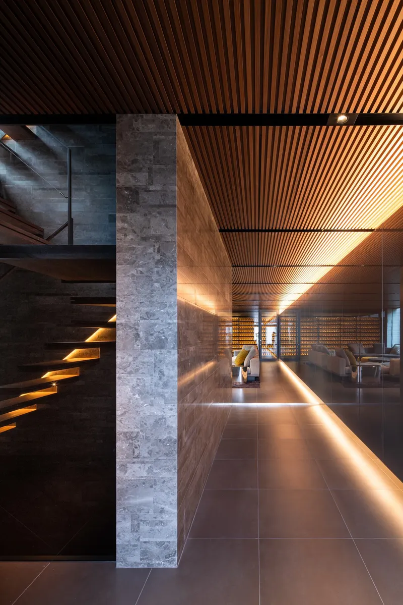 Interior corridor with timber slatted ceiling, stone column, and cantilevered staircase with integrated lighting