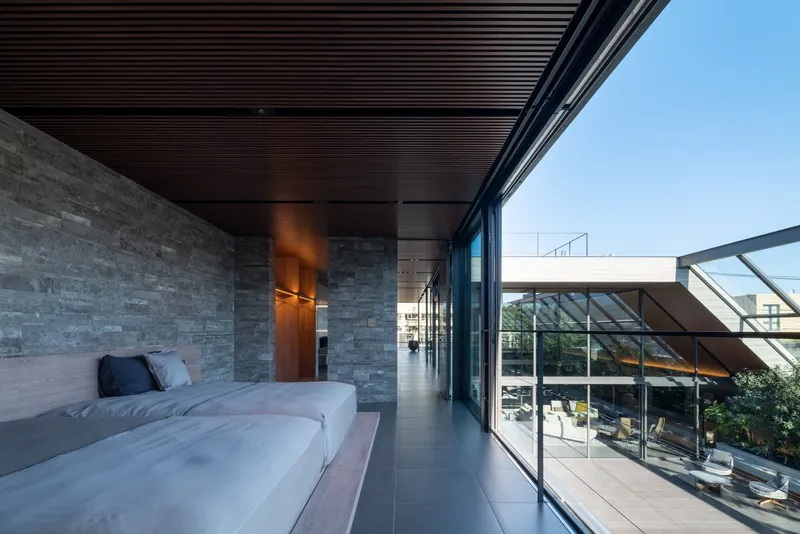 Bedroom terrace with stone wall and timber ceiling overlooking the glazed courtyard below
