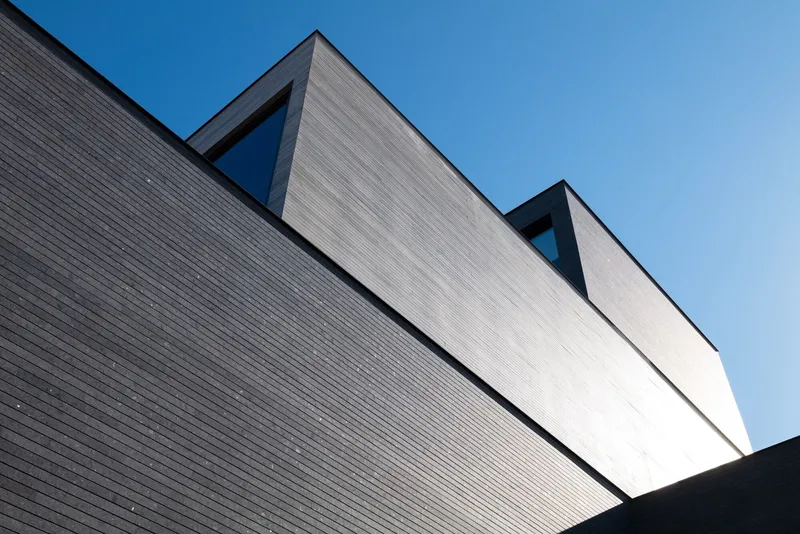 Upward view of ribbed cladding facade with angled roofline against blue sky