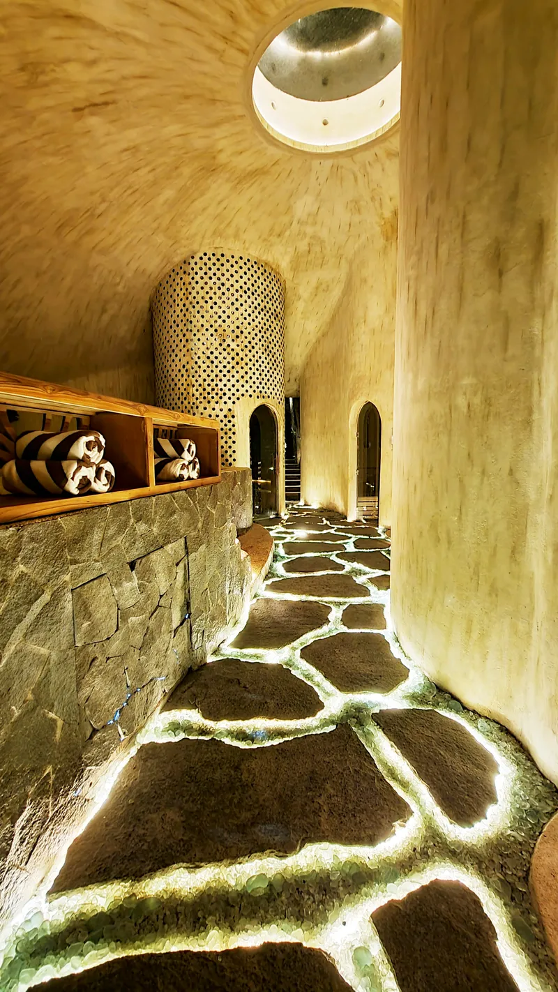 Corridor with irregular stone floor joints and perforated bamboo cylinder beneath a circular skylight