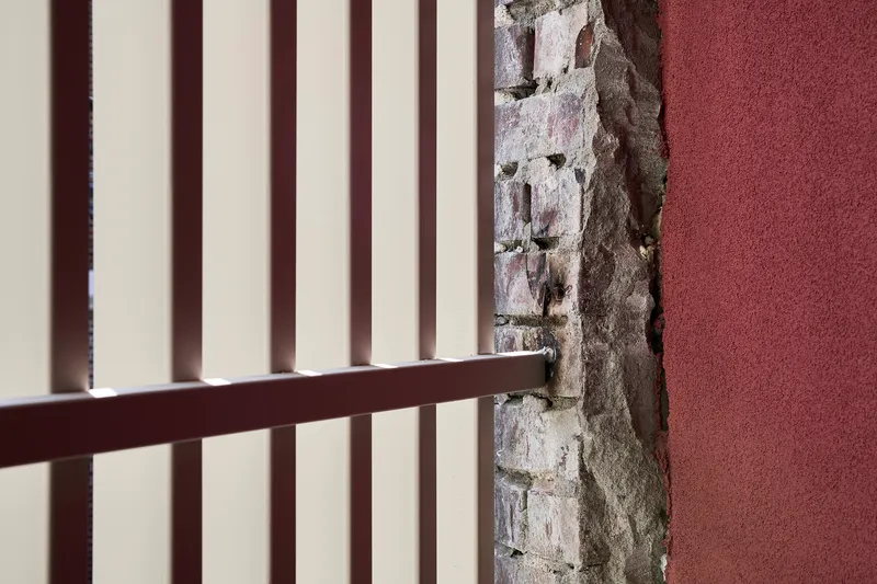 Detail of maroon metal railing meeting exposed whitewashed brick wall with rough mortar joints