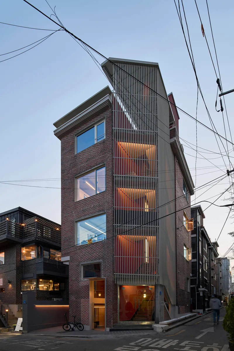 Street elevation of the vertical tower showing stacked windows and vertical metal screen at twilight