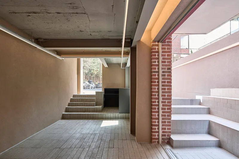 Interior entry hall with exposed concrete ceiling beams and two tiled staircases flanking a brick column