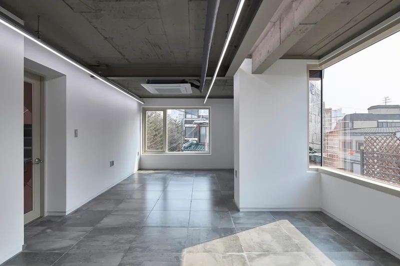 Open room with exposed concrete ceiling, linear lighting, and large-format grey floor tiles