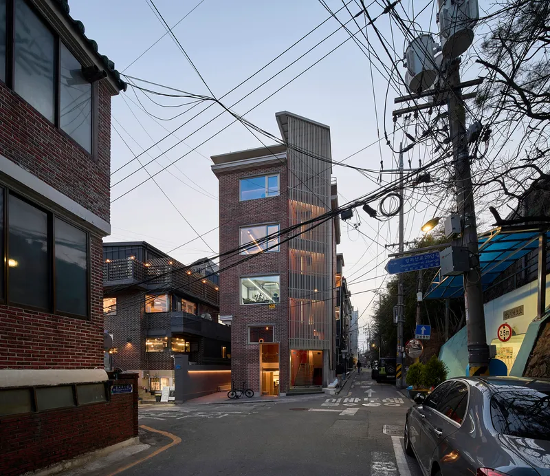 Narrow brick tower rising among low neighbors beneath a web of overhead utility wires at dusk