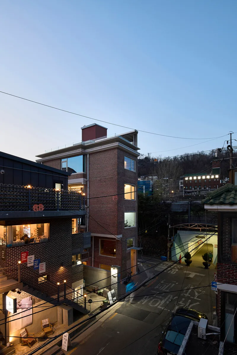 Slender brick facade overlooking adjacent courtyards and rooftops illuminated in the blue hour