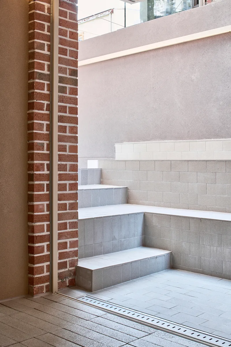 Corner stair with brick pilasters and white tile treads leading down to a linear drain
