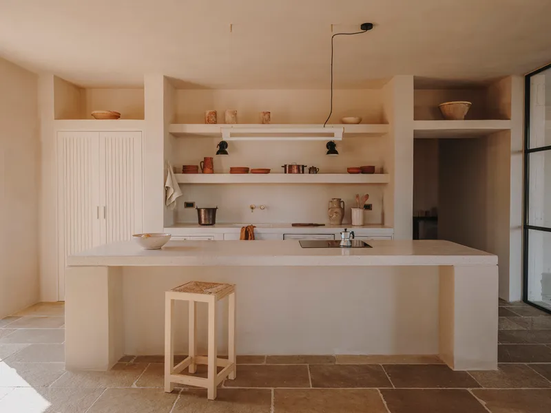 Kitchen with pale plaster island, open shelving and grooved cabinet doors on terracotta tile floor