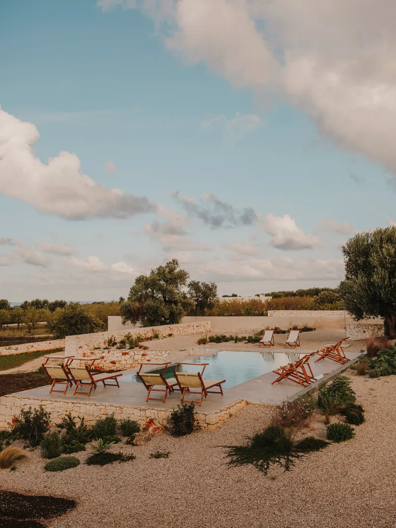 Swimming pool surrounded by canvas lounge chairs and native plantings under afternoon clouds