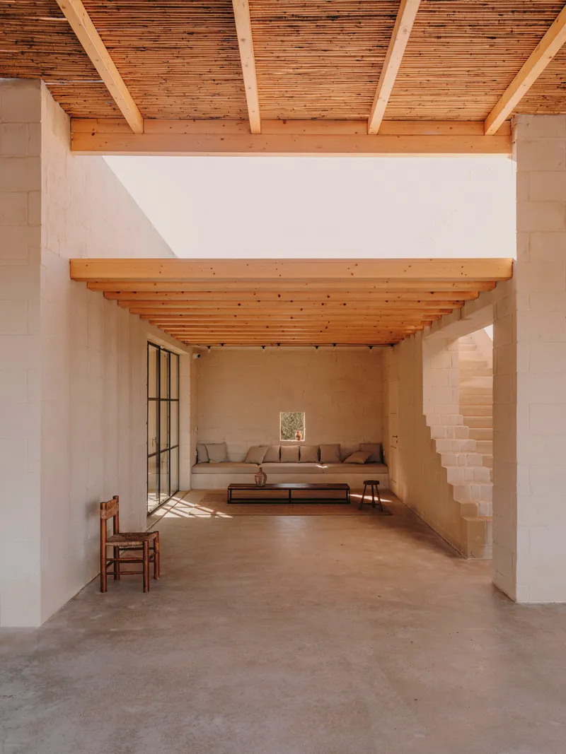 Interior space with exposed timber joists and beams connecting two seating areas in warm light