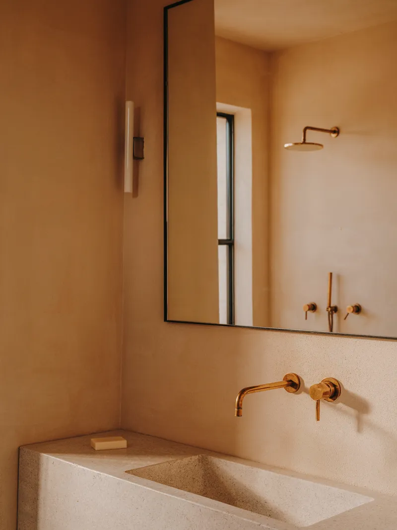 Bathroom vanity with integrated stone sink and brass wall-mounted faucet beneath a framed mirror