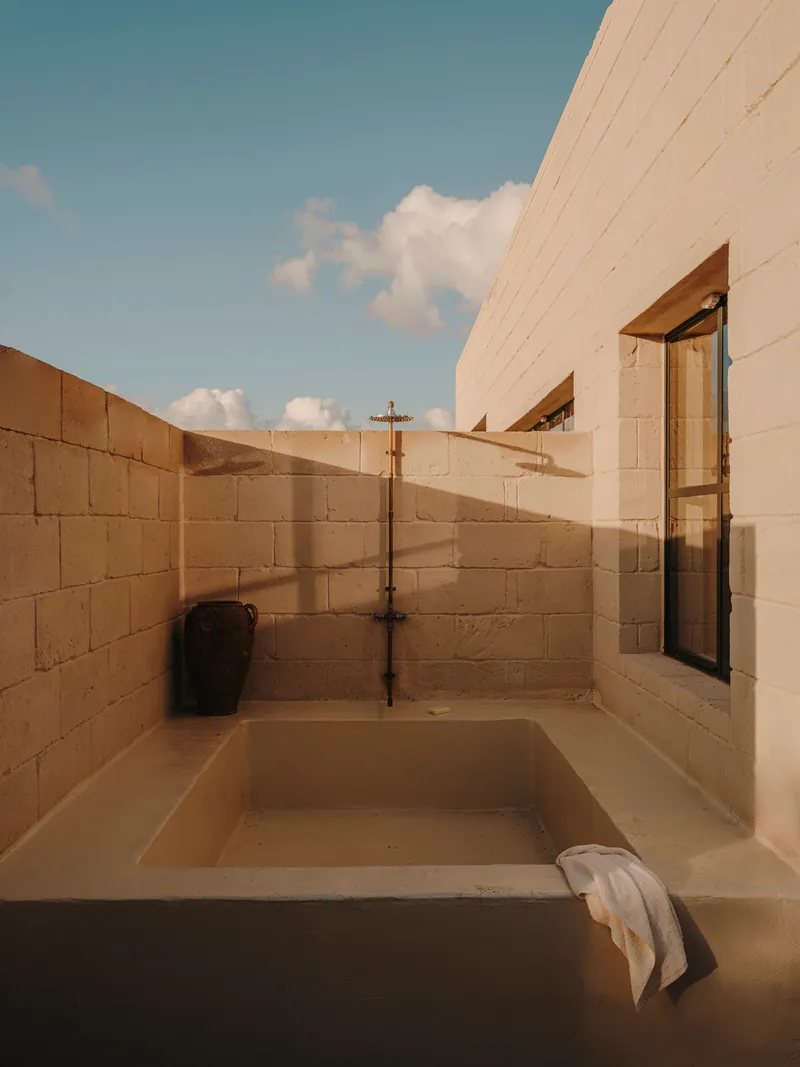 Outdoor sunken bathtub enclosed by concrete block walls with exposed brass plumbing under afternoon sky