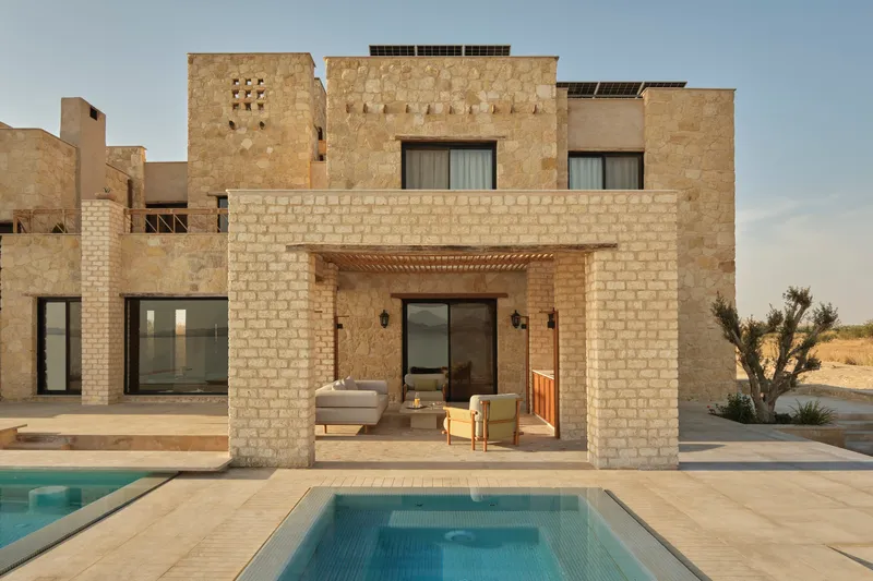Covered outdoor terrace with limestone columns framing the pool and desert landscape