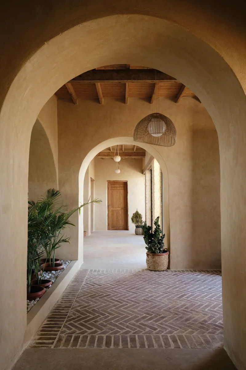 Sequence of plastered arches along a herringbone brick floor with potted plants