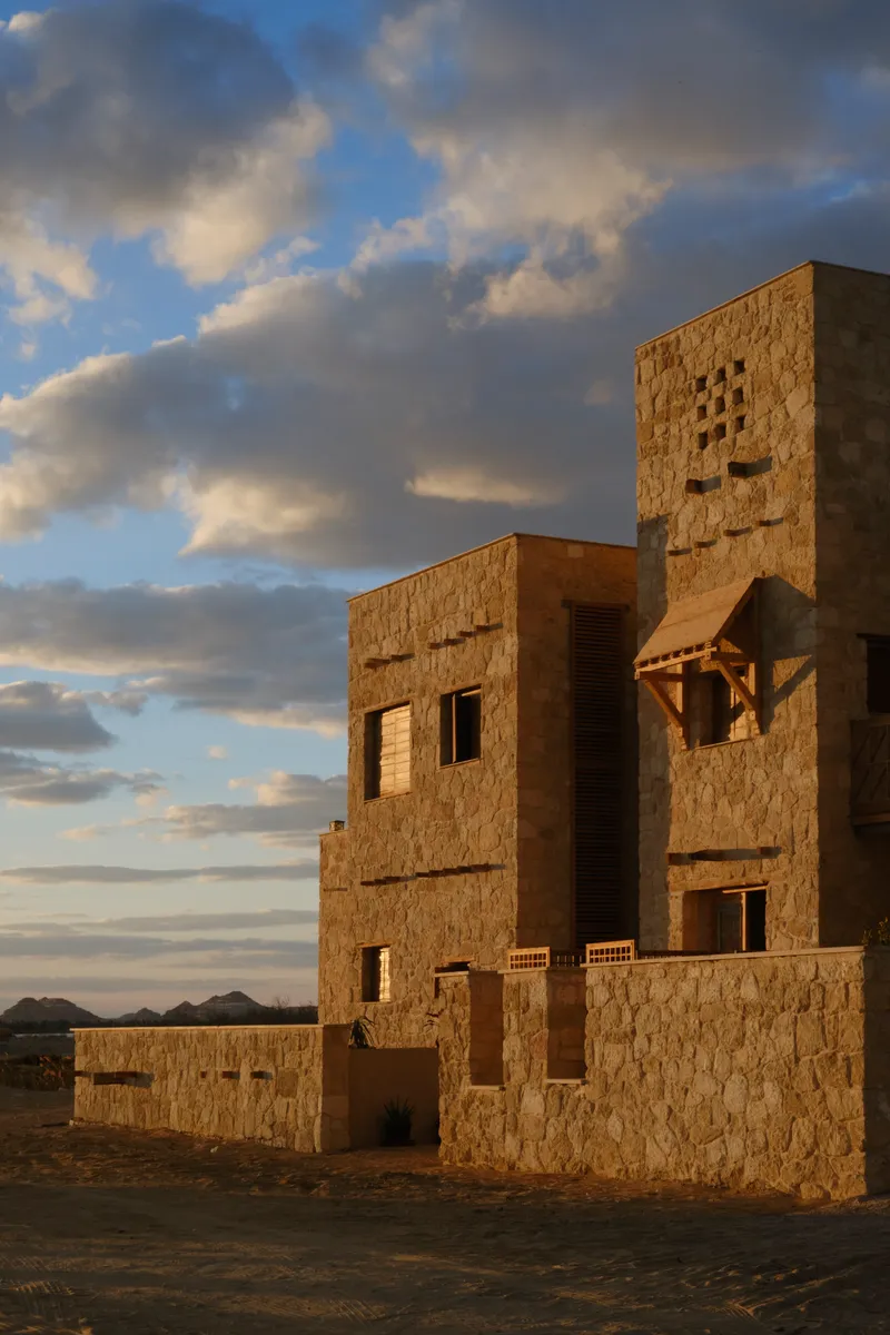 Stone block tower and connected volumes under a cloudy sky at sunset