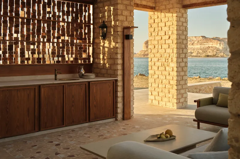 Open-air lounge with perforated brick screen wall and timber credenza overlooking calm water