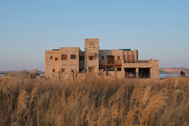 Rammed earth volumes with tower rising above golden grasses at dusk