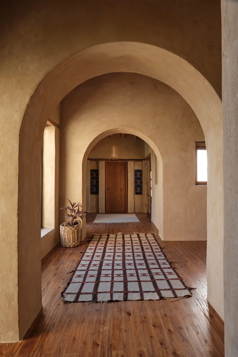 Corridor with nested barrel vaults and gridded runner rug leading to a timber door
