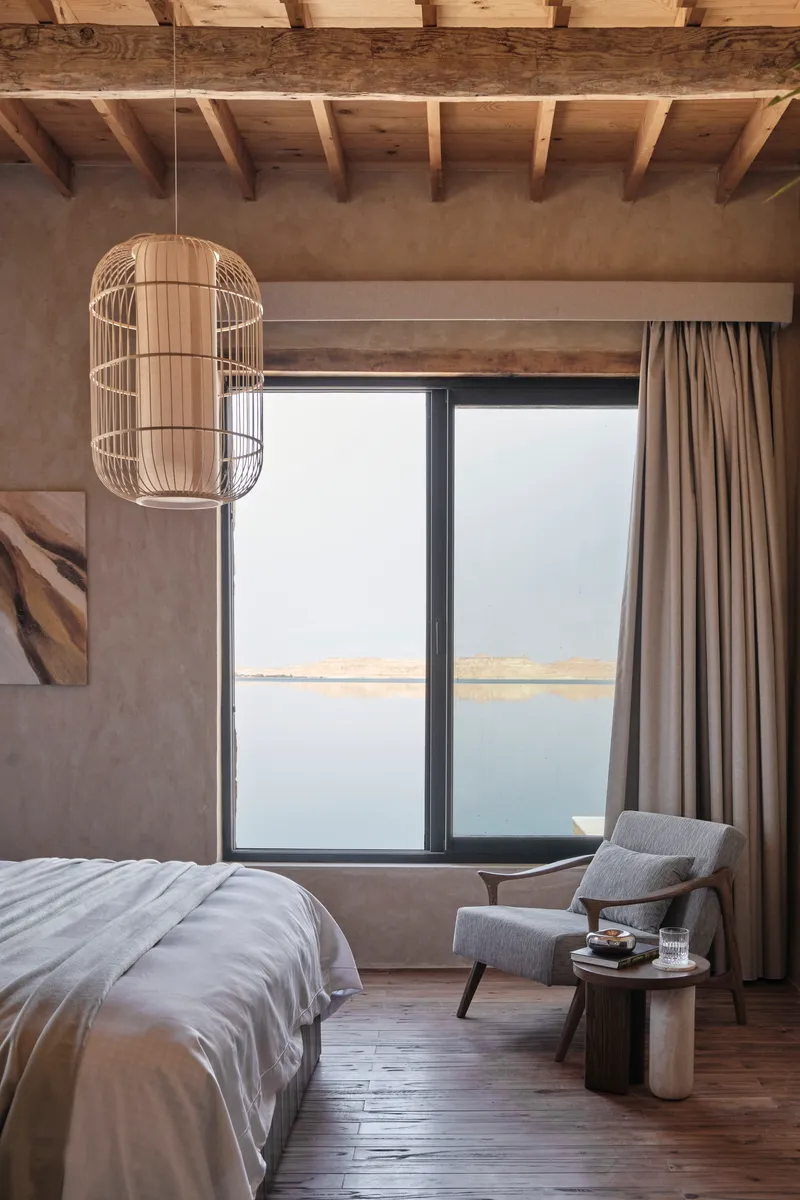 Bedroom interior with exposed timber ceiling joists and a cage pendant light beside the window