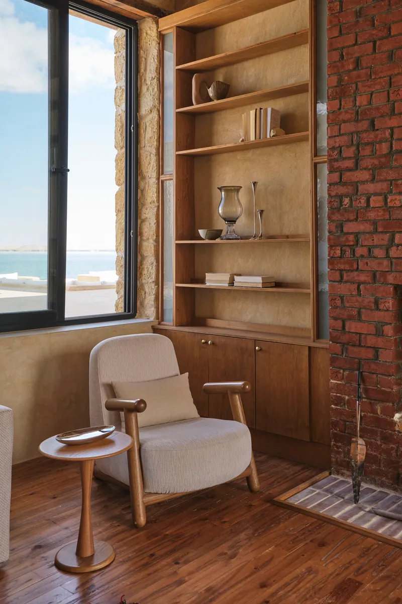 Built-in timber shelving unit next to exposed brick wall with an armchair near the open window