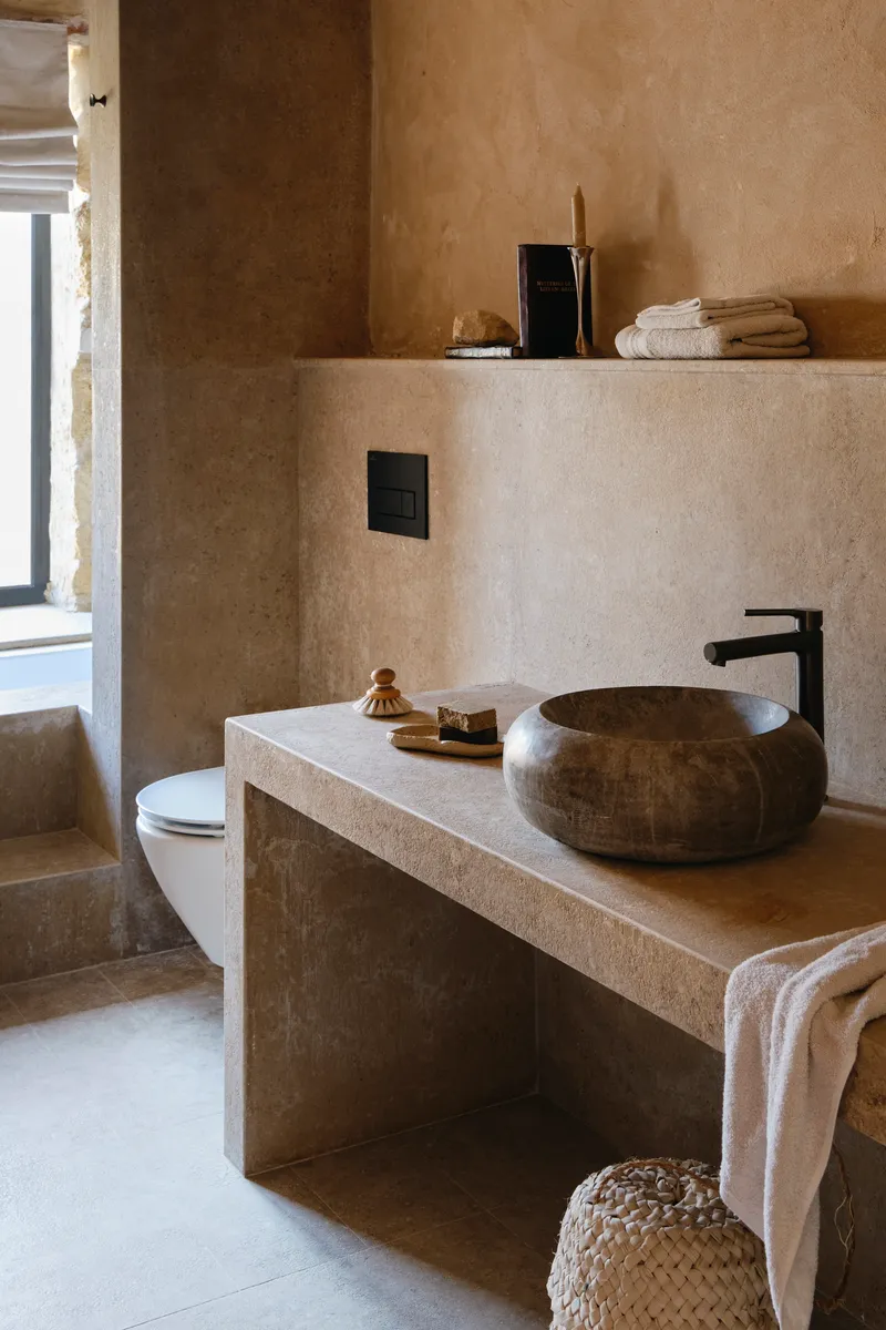 Bathroom vanity with rounded stone vessel sink and integrated floating shelf in textured plaster