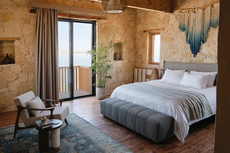 Bedroom with rough stone walls and timber balcony doors opening to daylight over the water