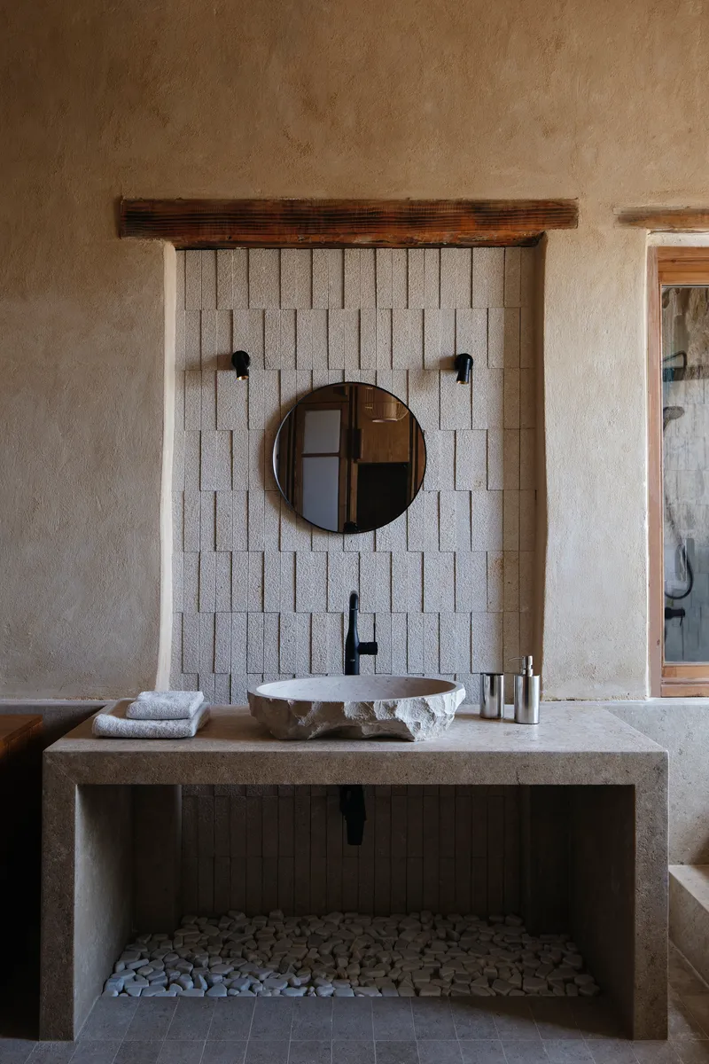 Concrete vanity console with white tile accent wall and circular mirror in textured plaster bathroom