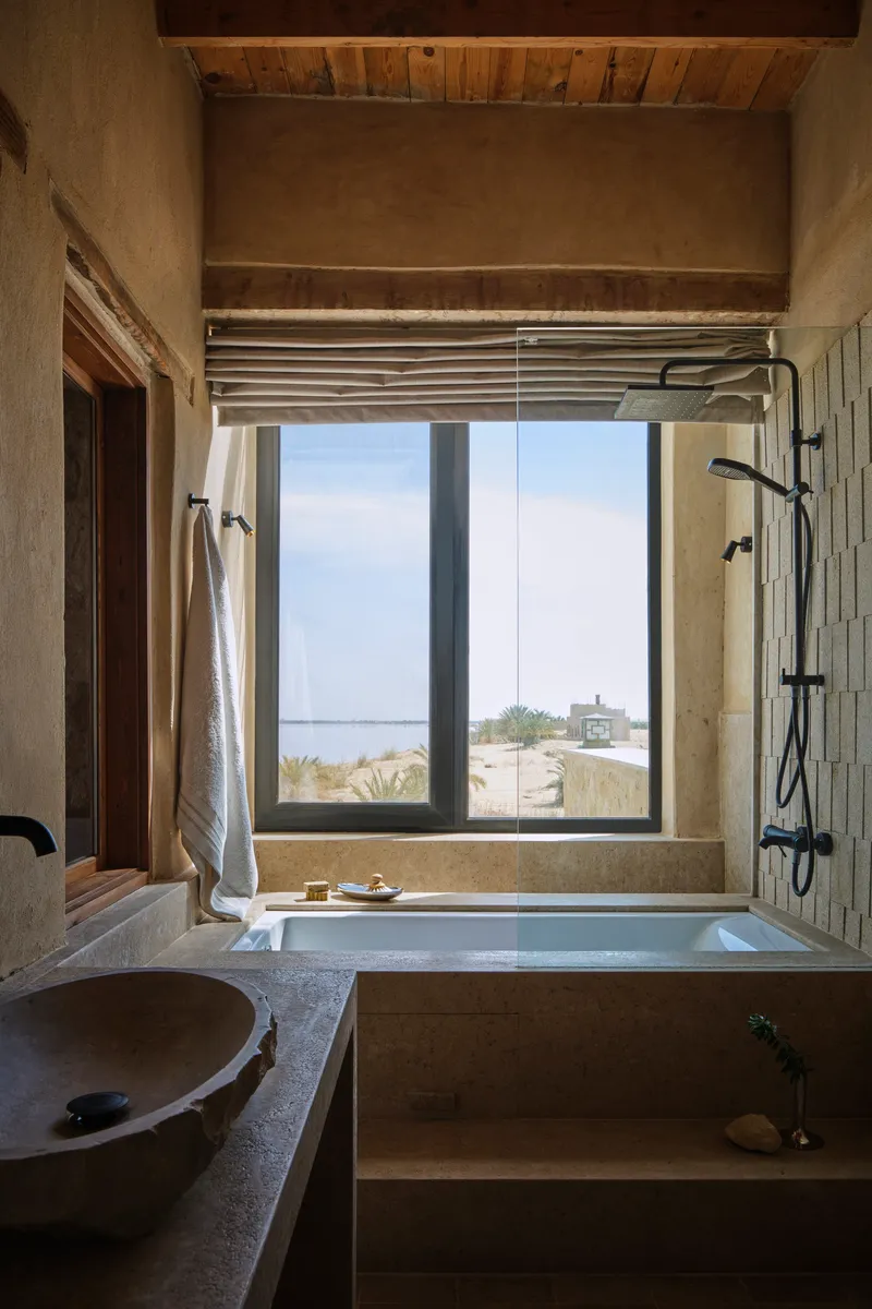 Bathroom with sunken tub and window framing coastal view with exposed timber ceiling above