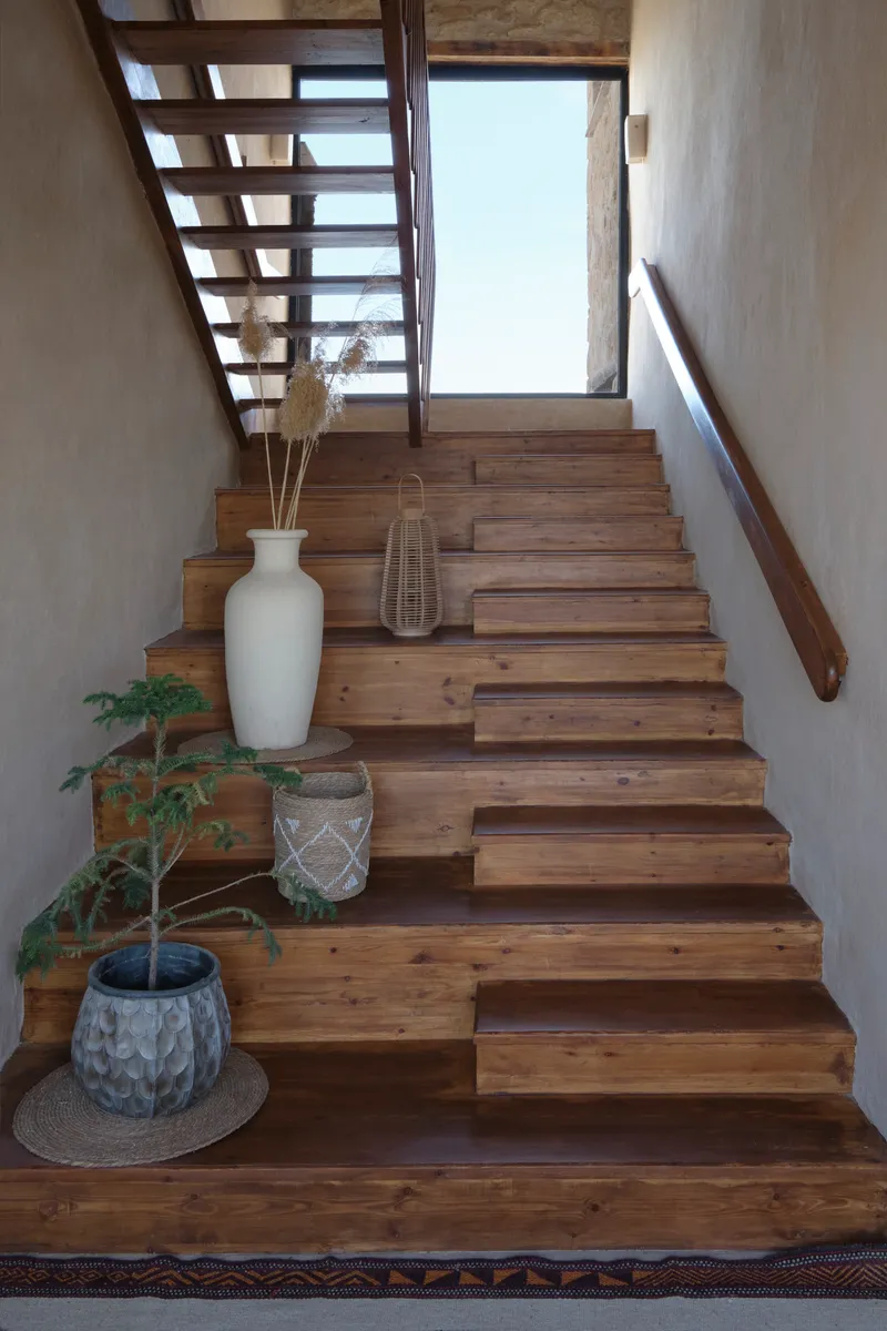 Timber staircase with open risers and planted vessels at base beside textured plaster walls