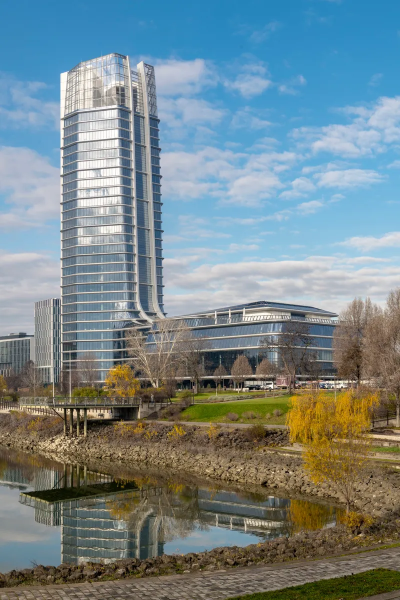 Waterfront view of the glass tower rising above the curved base with reflection in the foreground pond