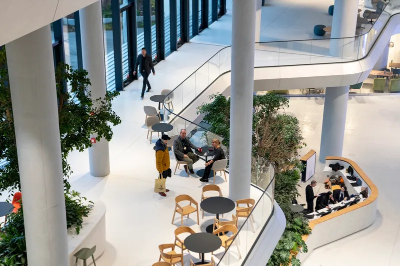 View down into the atrium showing curved balconies with seating areas, planters, and people gathered in conversation