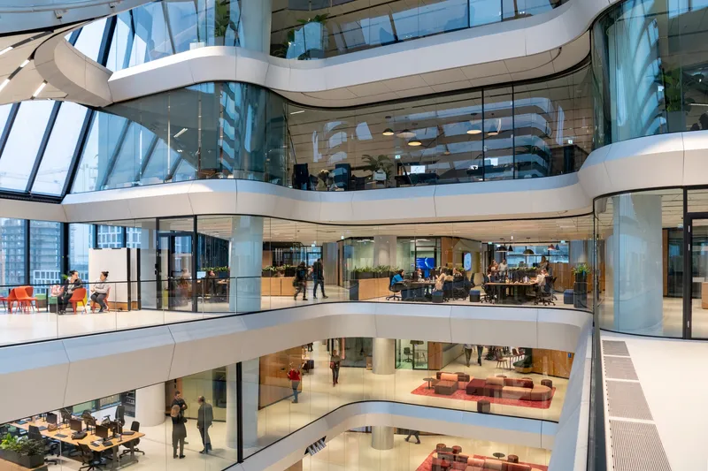 View into the spiraling atrium with curved white floor plates and glass-walled offices visible through the glazing