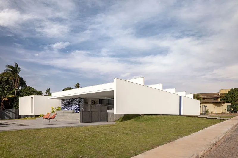 Street view of the white stucco facade with dark tiled portal and low concrete bench under palm trees