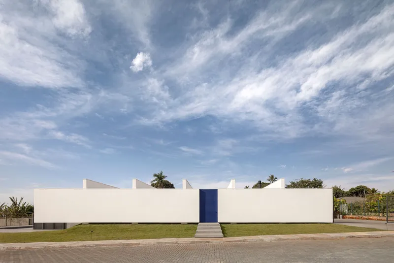 Long white facade with central blue door and stepped roofline against a cirrus cloud sky