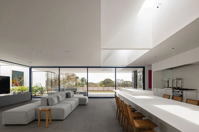 Open-plan living space with floor-to-ceiling glazing opening to lawn and double-height skylit void above